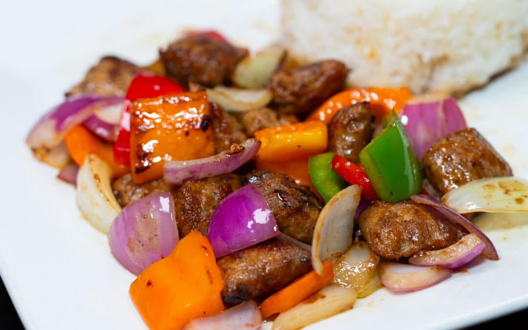 Close-up of Vietnamese Shaking Beef (Bò Lúc Lắc) served with white rice. Tender marinated beef cubes are stir-fried with colorful bell peppers, red onions, and aromatic seasonings, creating a vibrant and savory dish.